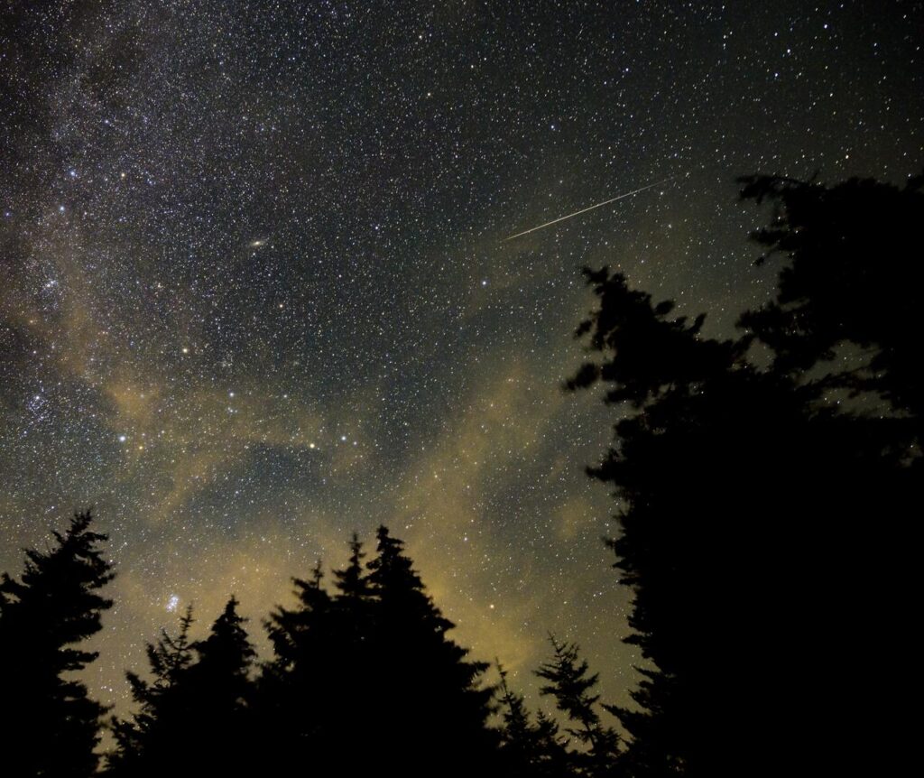 Ciel nocturne strié d'un météore au-dessus d'un paysage sombre