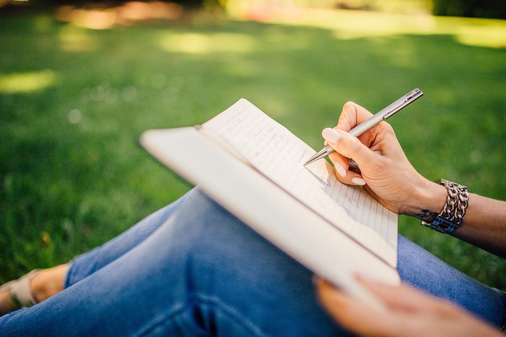 Personne assise dans l'herbe en train d'écrire dans un carnet