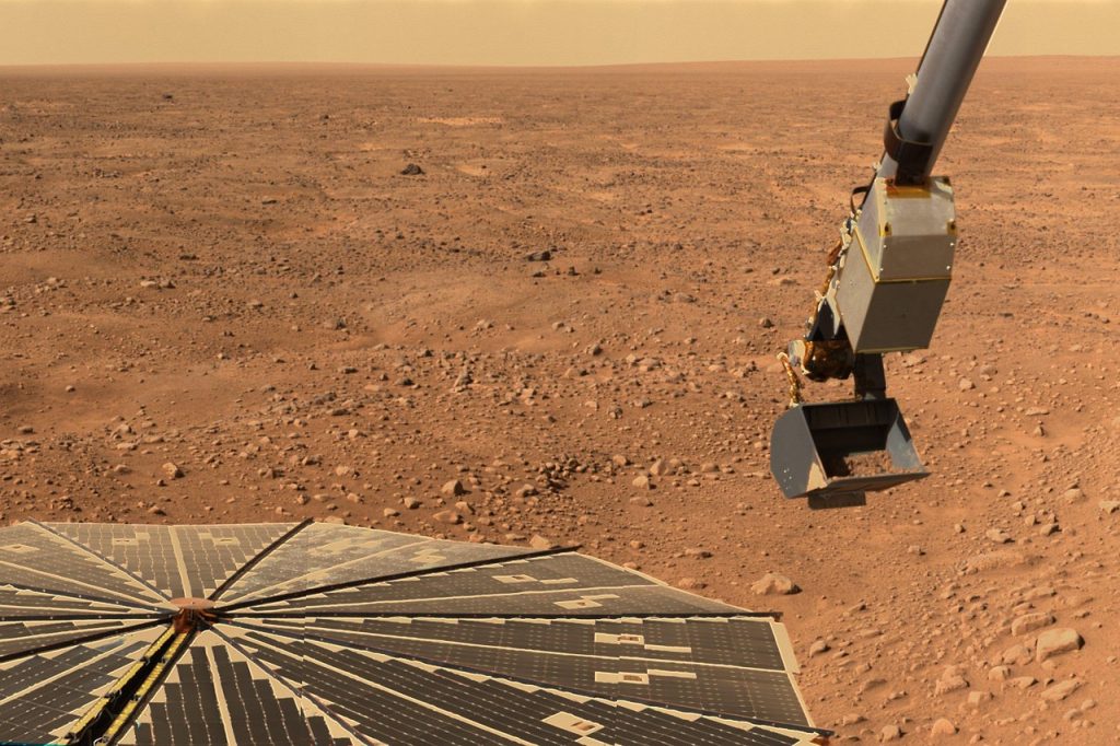Bras robotisé d'un rover posé sur le sol rouge de Mars