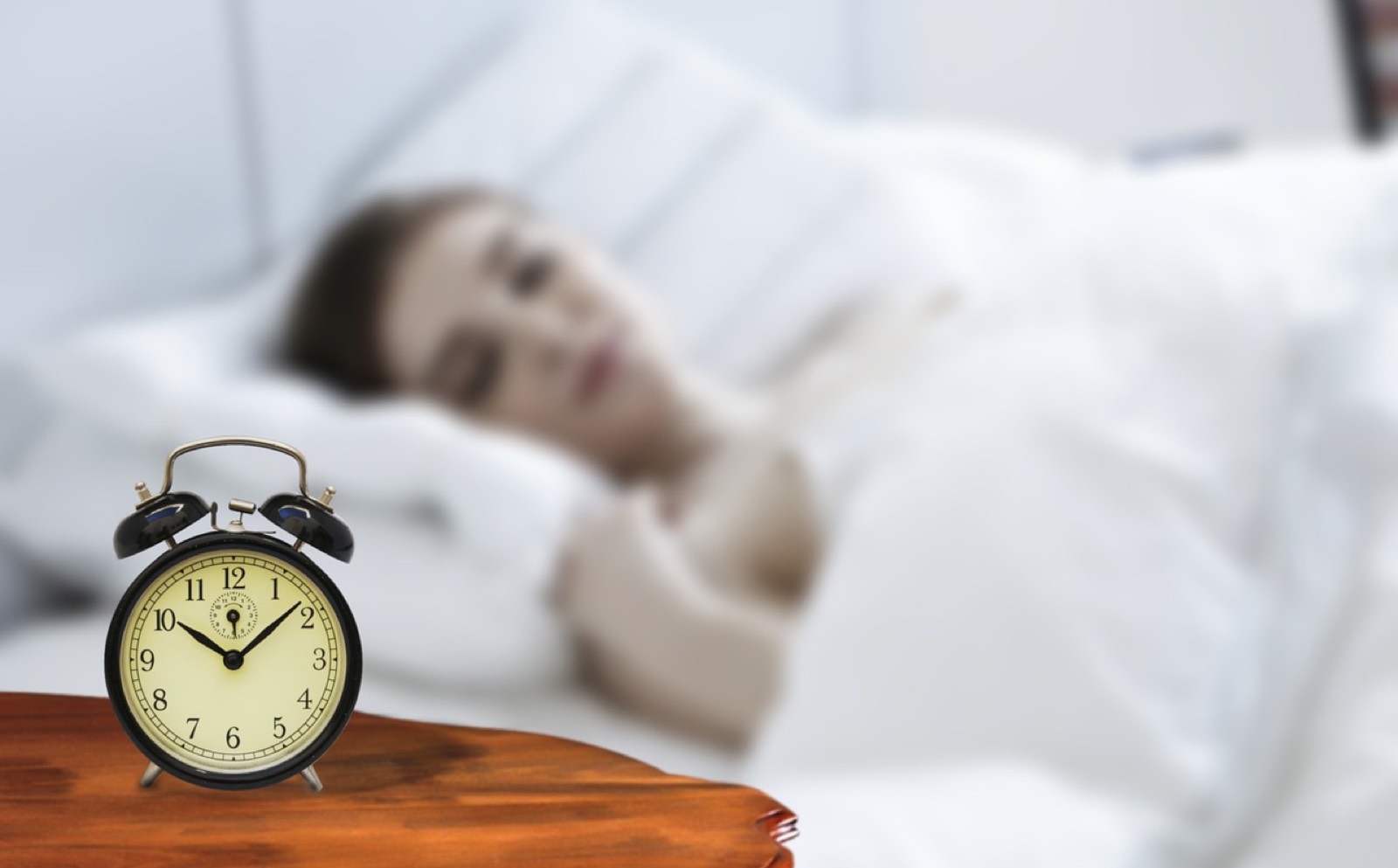 Femme éveillée dans son lit, réveil visible sur la table de nuit